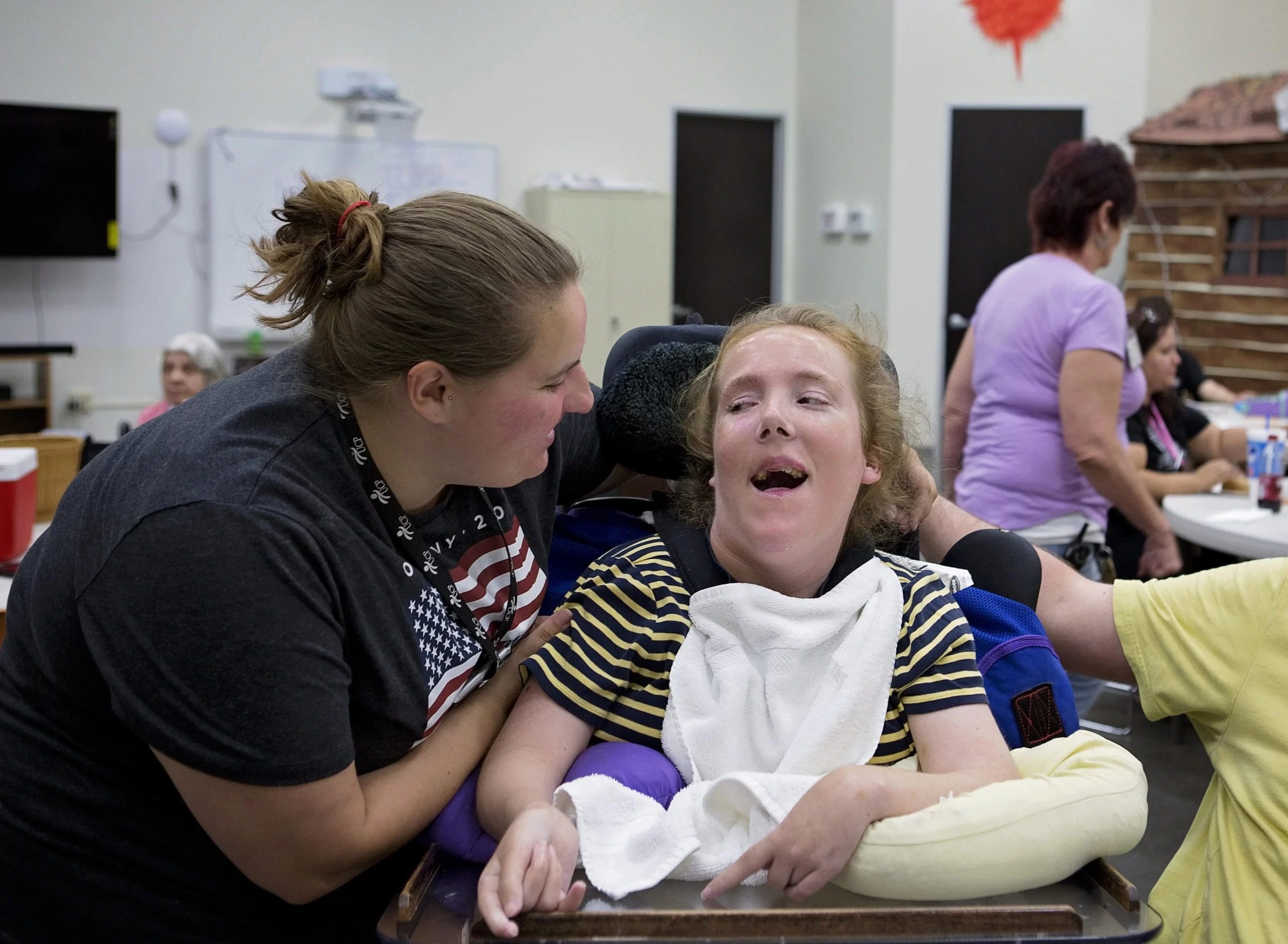 A girl receiving pediatric therapy in a wheelchair is assisted by a woman in a wheelchair at an early learning center.