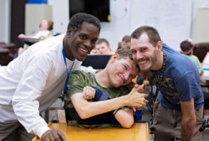 Three men and a boy with cerebral palsy of Arizona posing in a pediatric therapy classroom.