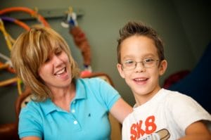 A young boy with cerebral palsy of Arizona smiles during pediatric therapy in a playroom.