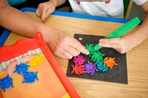 A child with cerebral palsy of Arizona is using scissors during pediatric therapy to cut shapes out of paper.