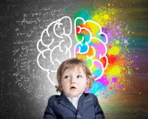 A young boy with cerebral palsy is standing in front of a chalkboard at an early learning center.