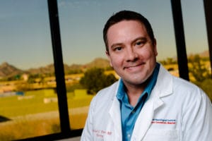 A smiling man in a lab coat conducting day treatment for adults at Cerebral Palsy of Arizona.