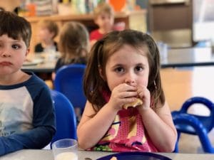 Two children with cerebral palsy eating at a table in an early learning center.