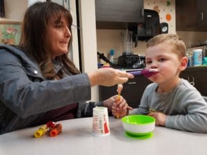 A woman is engaging in pediatric therapy by feeding a child with a spoon.