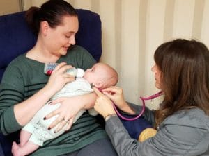 A woman is holding a baby while providing pediatric therapy.
