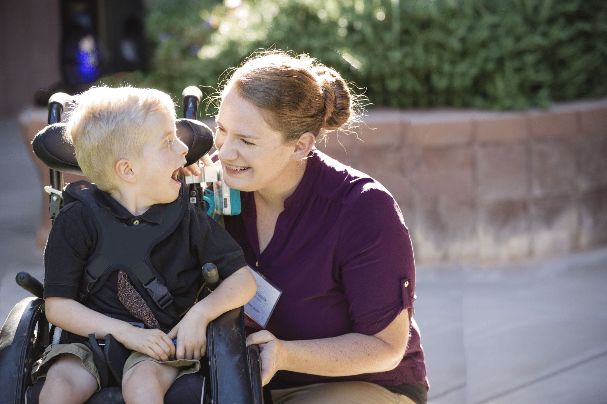 A woman with cerebral palsy of Arizona guiding a boy in a wheelchair at an early learning center.