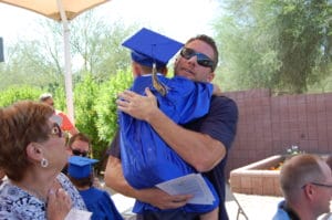In a heartwarming scene, a man in a blue graduation cap embraces a young boy in need of pediatric therapy for cerebral palsy at the day treatment center in Arizona.
