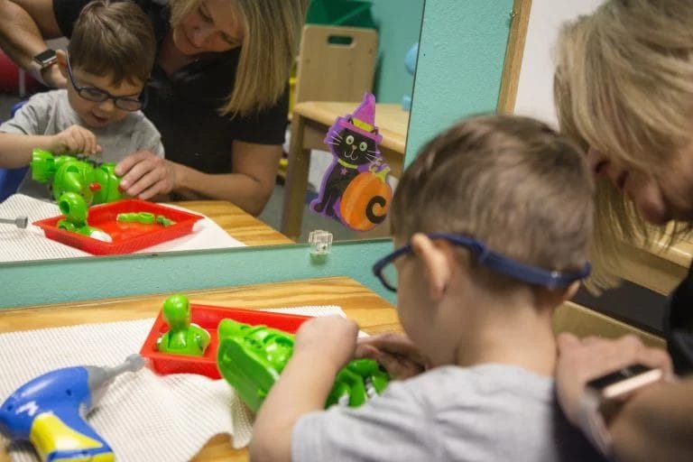 A woman is providing pediatric therapy to a child in a playroom.