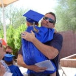 A man in a graduation cap and gown is hugging a young boy at an early learning center.