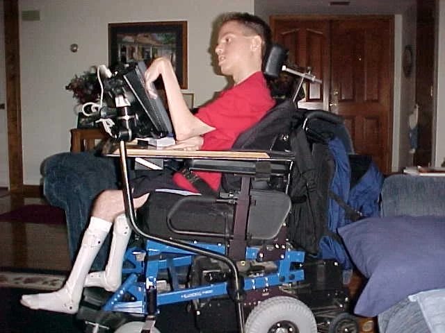 A wheelchair-bound man utilizing a laptop for home-based community services.