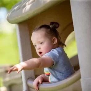 A little girl with cerebral palsy of Arizona peeks out of a playhouse, benefiting from home and community based services and pediatric therapy.