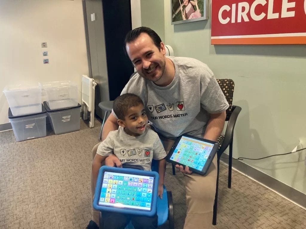 A man and a child sitting on a blue chair engaging in pediatric therapy with ipads.