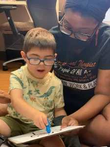 A woman at a pediatric therapy session is reading a book to a young boy with cerebral palsy of Arizona.