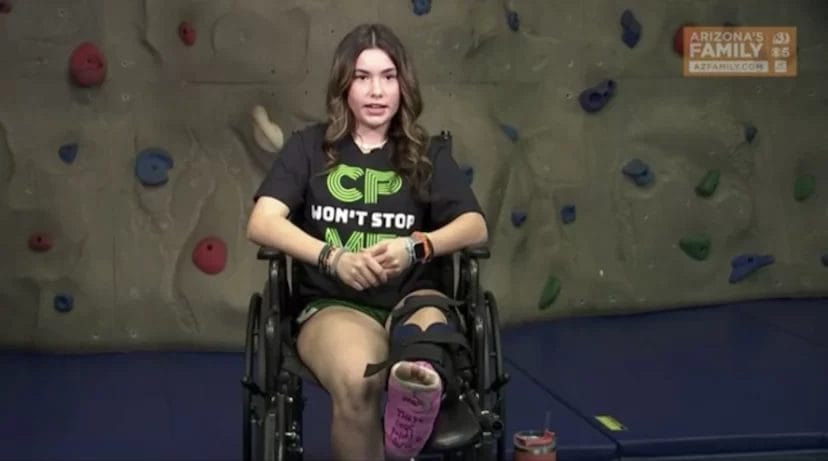 A woman in a wheelchair receiving pediatric therapy in front of a climbing wall.