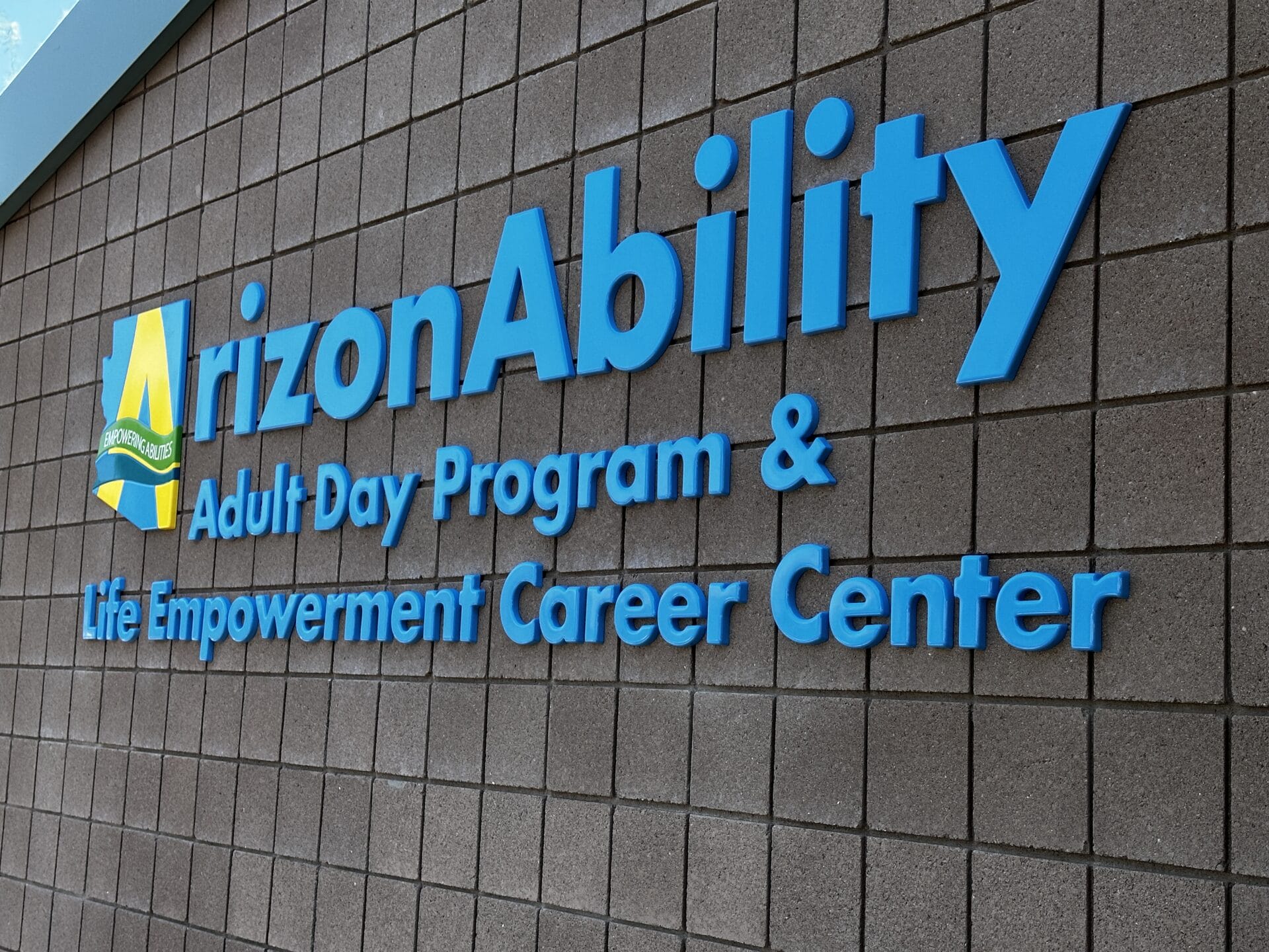 Sign for ArizonAbility Adult Day Program & Life Empowerment Career Center, proudly affiliated with UCP of Central AZ, mounted on a tiled wall.