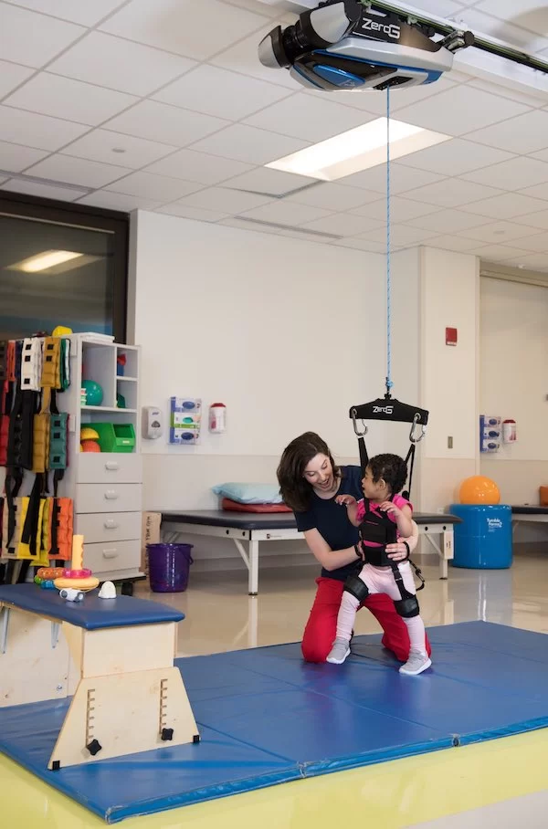 A woman is providing pediatric therapy to a child on a swing in an early learning center.