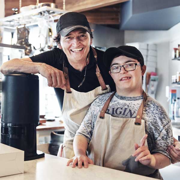 An apron-clad man and a young boy enjoying a coffee shop outing.