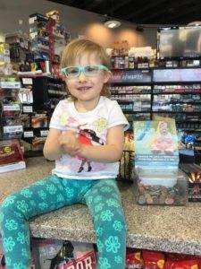 A little girl in glasses sitting at the counter of a pediatric therapy store.