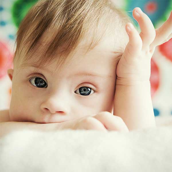 A baby with blue eyes laying on a blanket at an early learning center.