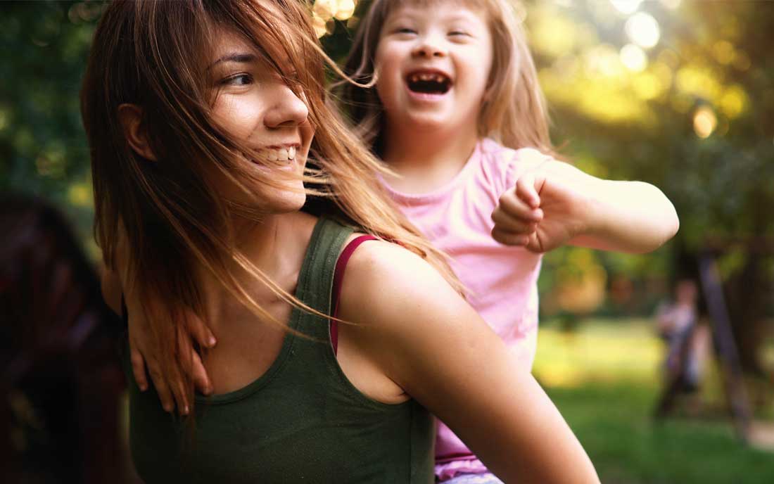 A woman and a little girl with cerebral palsy laughing in a park.